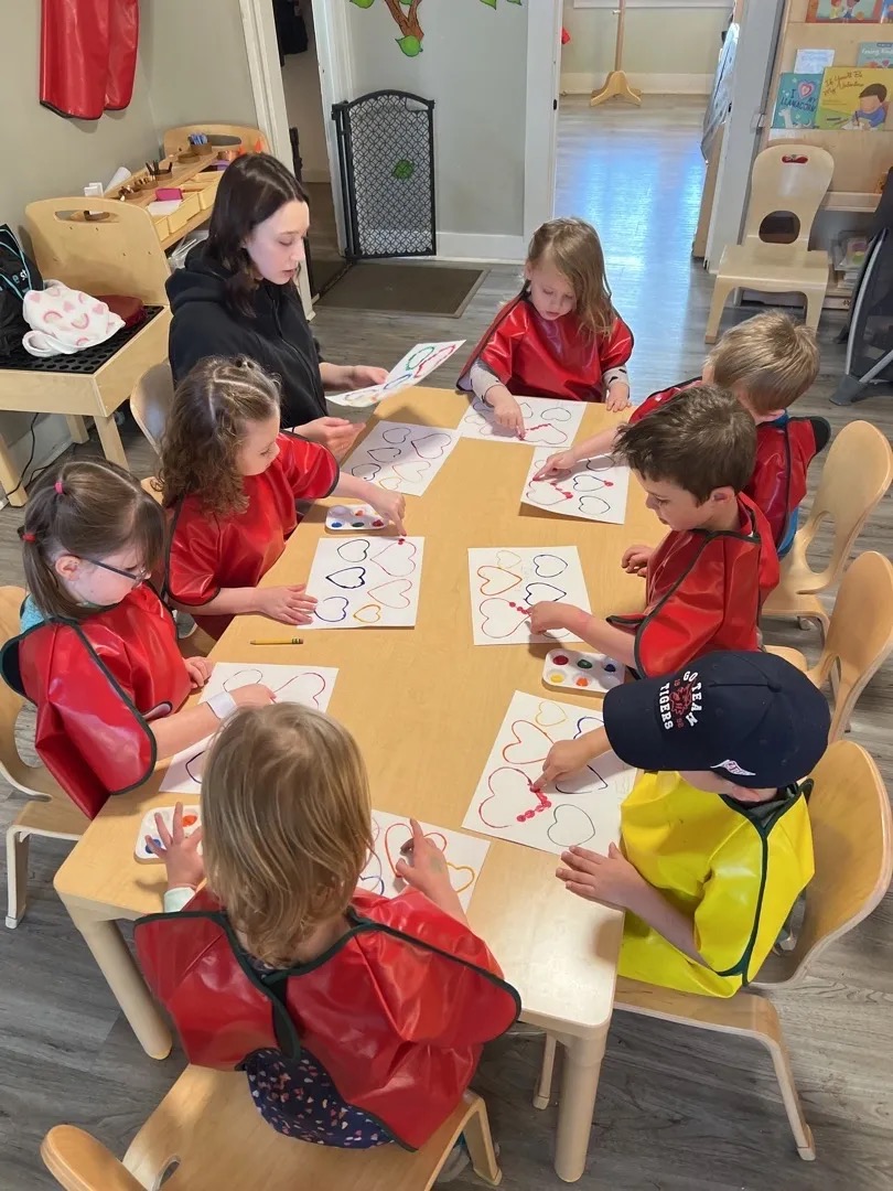 A Silly Billies educator leading a small-group heart-painting project with preschool children