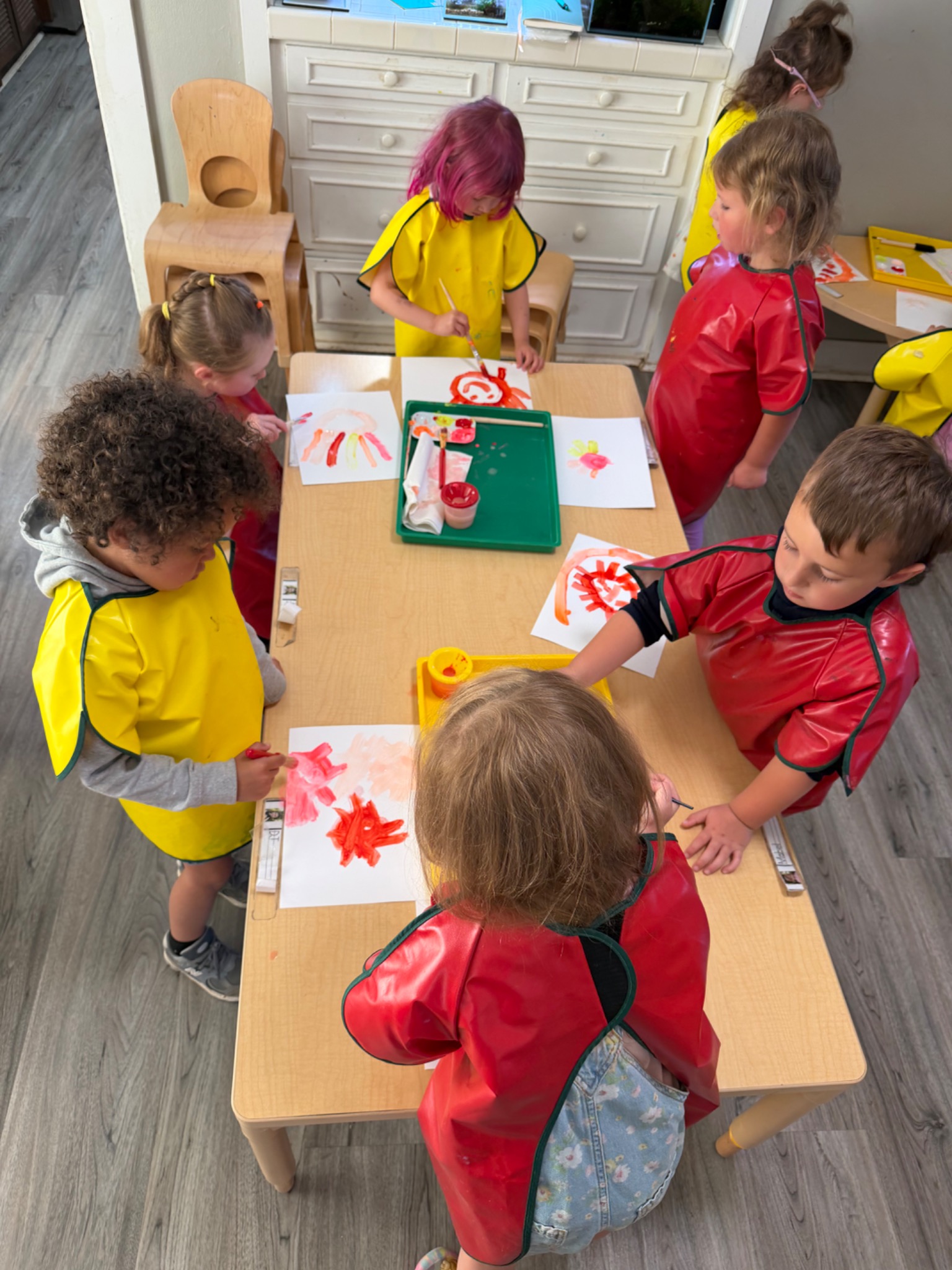 Preschool children exploring red and yellow paint together at a classroom table